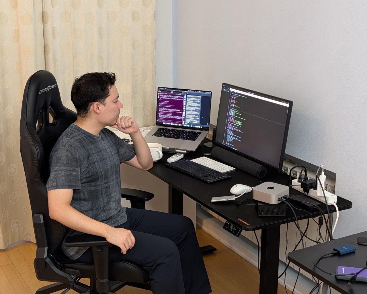 Tim at his desk, working at a laptop and a monitor full of code